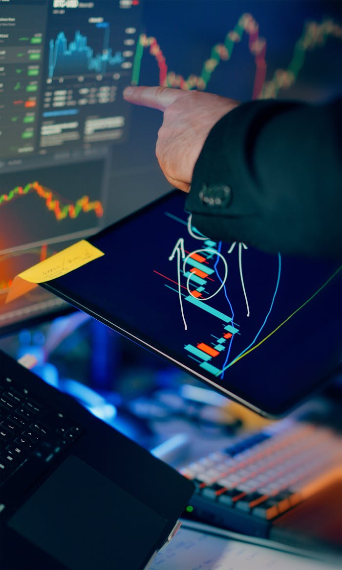 A business professional examines financial charts on a tablet and monitor for investment strategy.