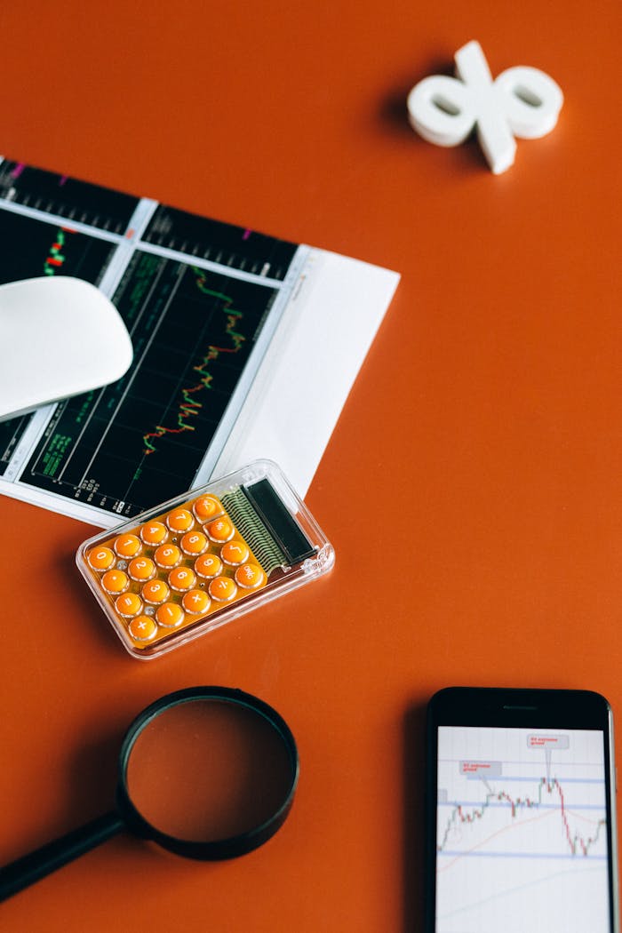 Desk setup with calculator, graphs, and tools on orange surface for financial analysis.